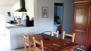 A dining area with a wooden table and chairs, a kitchen in the background, and a wooden cabinet.