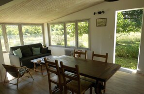 En matplats med ett träbord och stolar, en soffa med kuddar och stora fönster som ger utsikt över omgivningen.