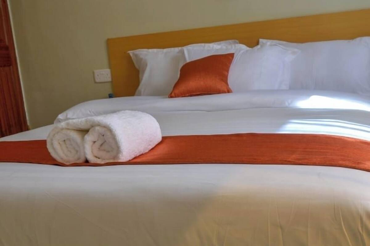 A neatly made bed with white linens, an orange bedspread, and a folded white towel.