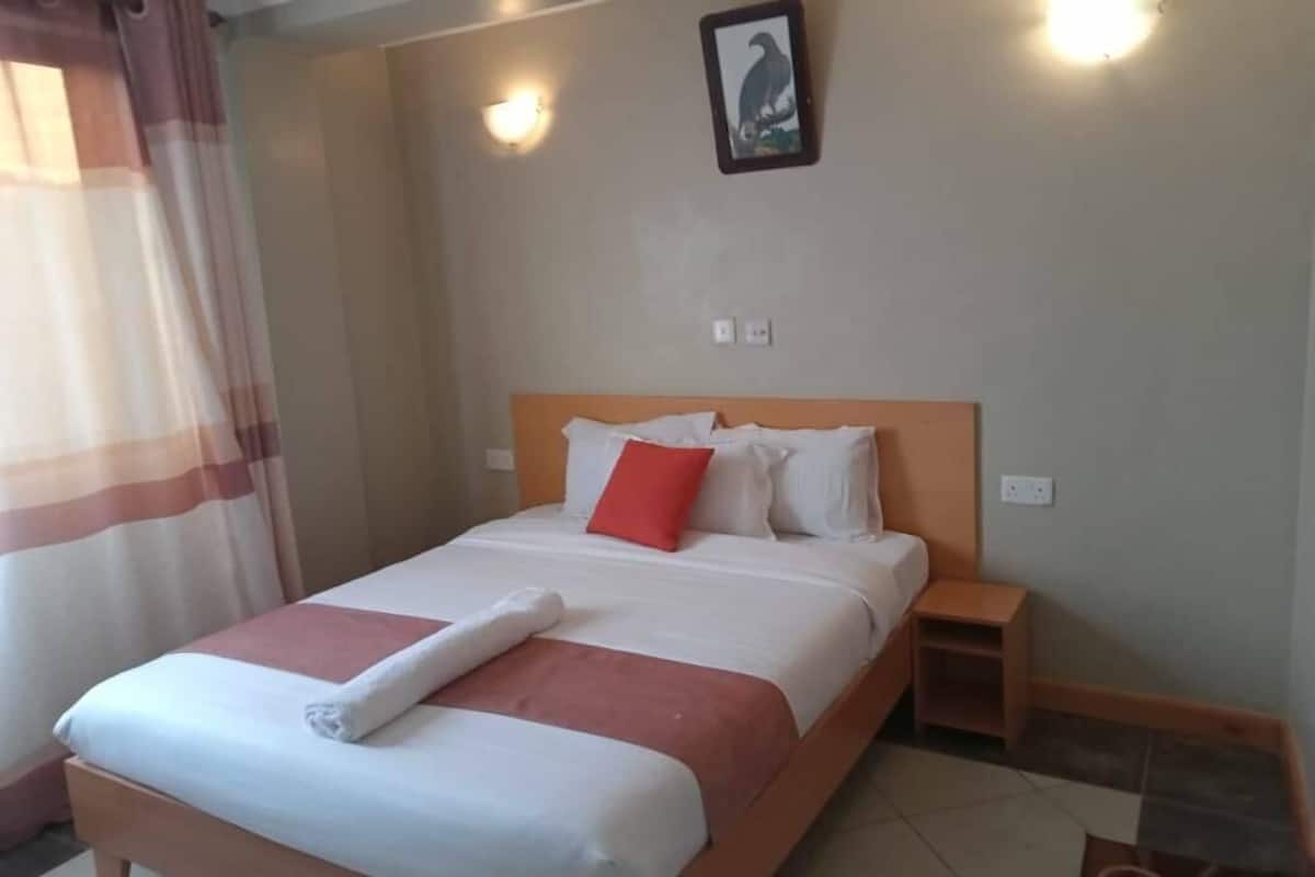 A neatly made bed with a red pillow, a wooden headboard, and a nightstand to the right.