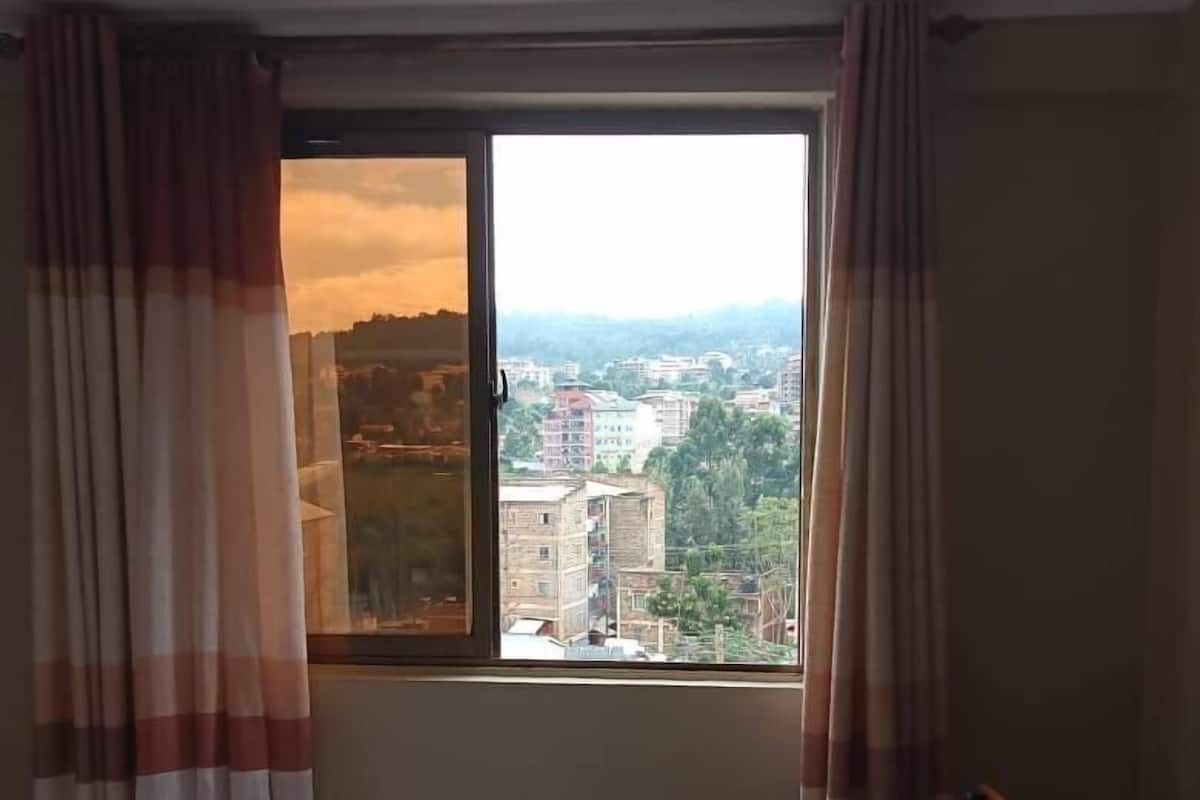 A hotel room with a bed, a wooden chair, and a window with curtains.
