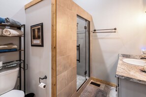 Un bagno con un water, un lavandino, una doccia con pareti in vetro e scaffali con asciugamani.