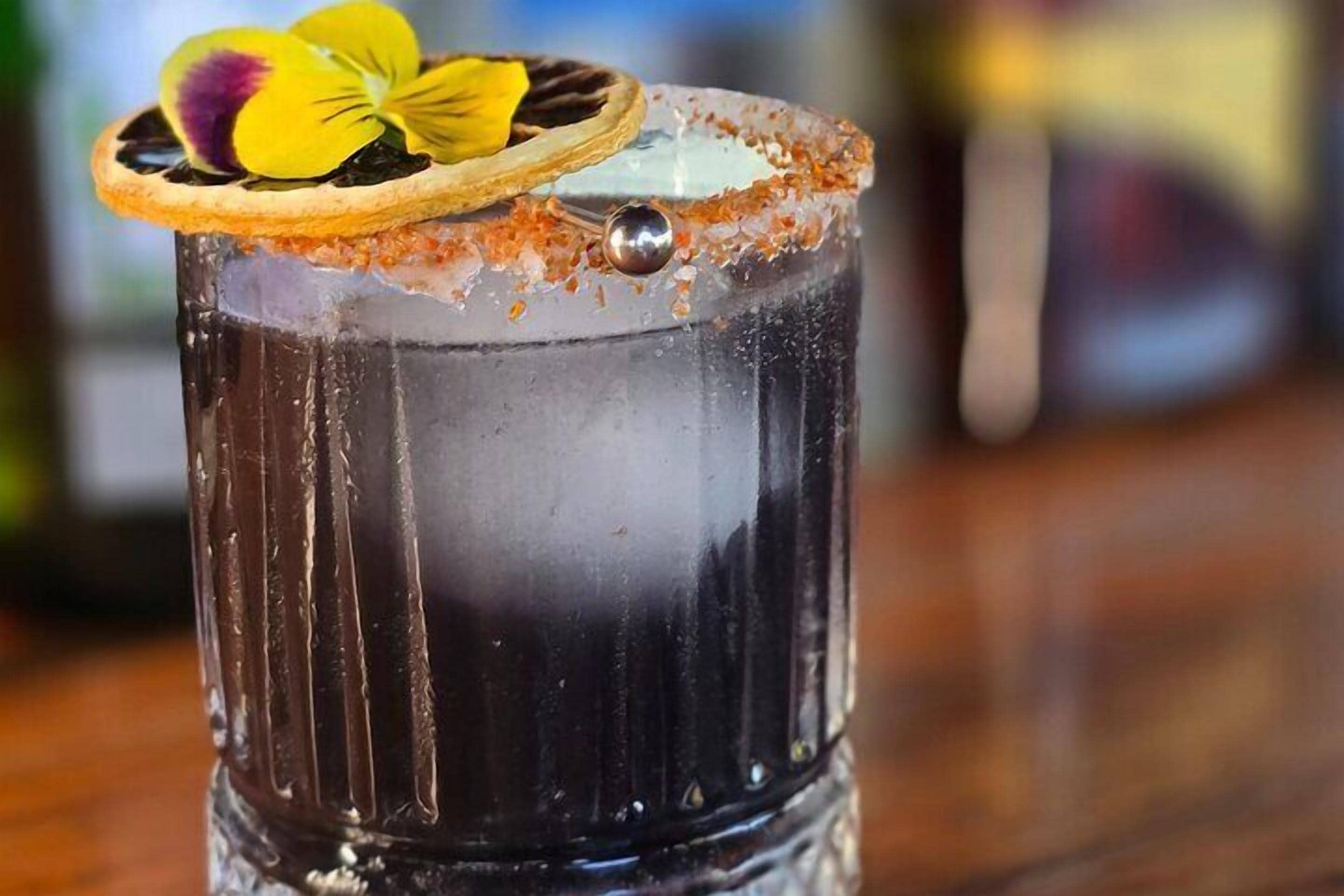 Un vaso de cóctel con borde de sal, adornado con una flor y una cereza.