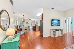 A spacious living area with hardwood flooring, a dining table, and a kitchen in the background.