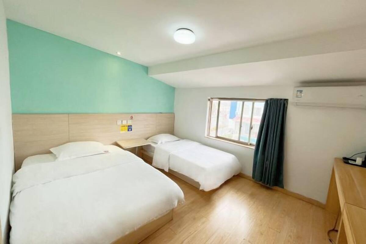 A hotel room with two beds, a window with curtains, a wooden headboard, and a desk with a lamp.