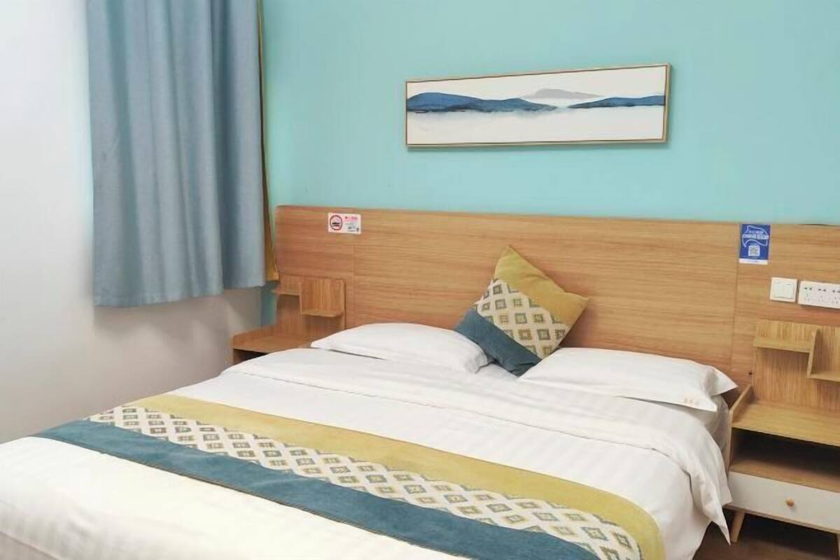 A neatly made bed with a patterned bedspread, a headboard, and a wall-mounted painting.