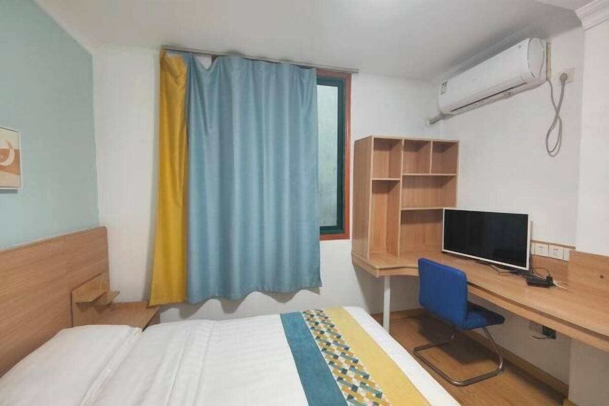 A room with a bed, a desk with a computer, a chair, a TV, and an air conditioning unit.