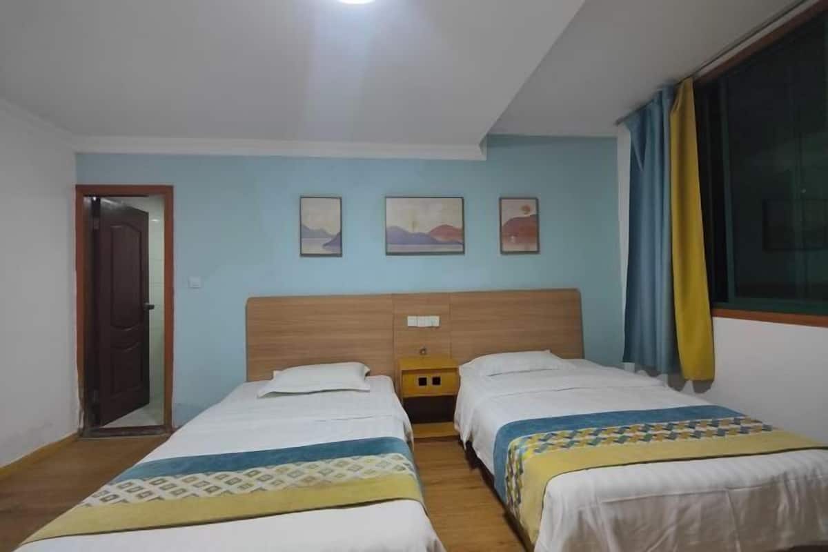 A room with two beds, a wooden headboard, a small bedside table, and a window with curtains.
