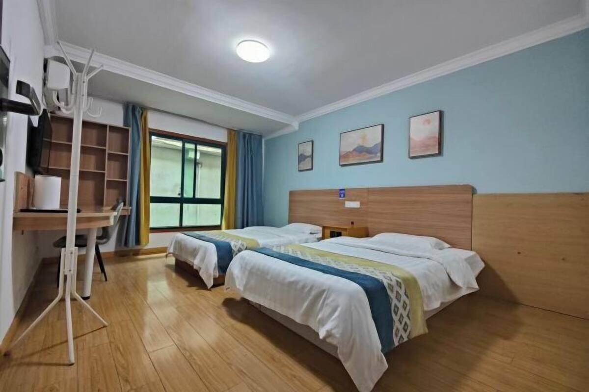 A hotel room with two beds, a wooden headboard, a desk with a chair, and a window with curtains.