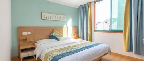 A bedroom with a bed, bedside tables, a nightstand, a window with curtains, and a wall-mounted artwork.
