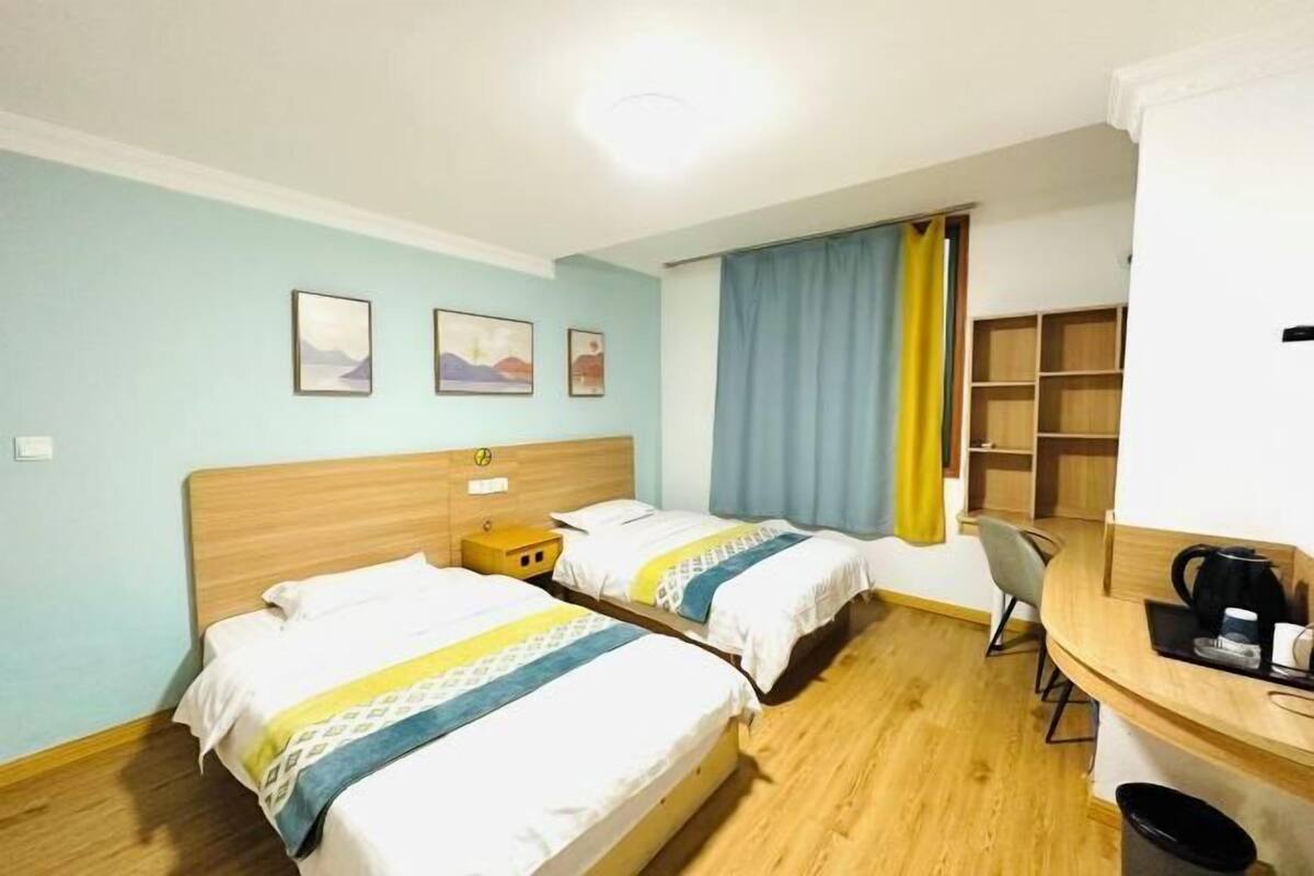 A hotel room with two beds, a desk, a chair, and a small table with a coffee maker.
