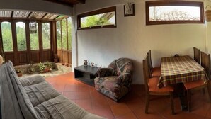 A cozy living room with a sofa, a patterned armchair, a dining table with chairs, and a kitchen area with a stove and cabinets. - Hostal Renacer  (Villa de Leyva)