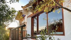 A rustic house with a stone foundation, wooden deck, and large windows. - Hostal Renacer  (Villa de Leyva)