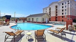 Un hôtel doté d’une piscine, de chaises longues et d’un petit bâtiment surmonté d’un toit rouge.