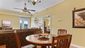 Un coin repas avec une table ronde en bois et des chaises, un ventilateur de plafond et un téléviseur en arrière-plan.