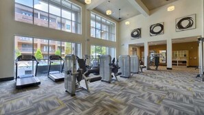 Ein Fitnessstudio mit Laufbändern, Kraftgeräten und einem gemusterten Boden.