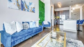 Ein modernes Wohnzimmer mit einem blauen Sofa, einem Glastisch und einer vertikalen, grünen Wandbegrünung.