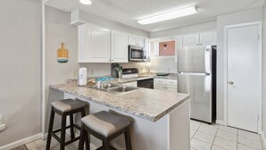 A modern kitchen with white cabinets, a granite countertop, stainless steel appliances, and two bar stools.