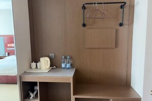 Ein kleines Hotelzimmer mit Schreibtisch aus Holz, einer kleinen Ablage für Toilettenartikel, einer Kleiderstange und einem Holzkoffer.