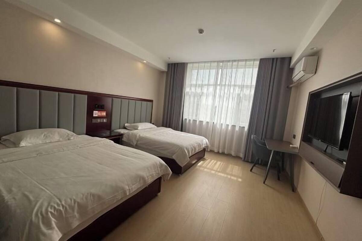 Une chambre d’hôtel avec deux lits, un bureau, une télévision et une fenêtre avec des rideaux.