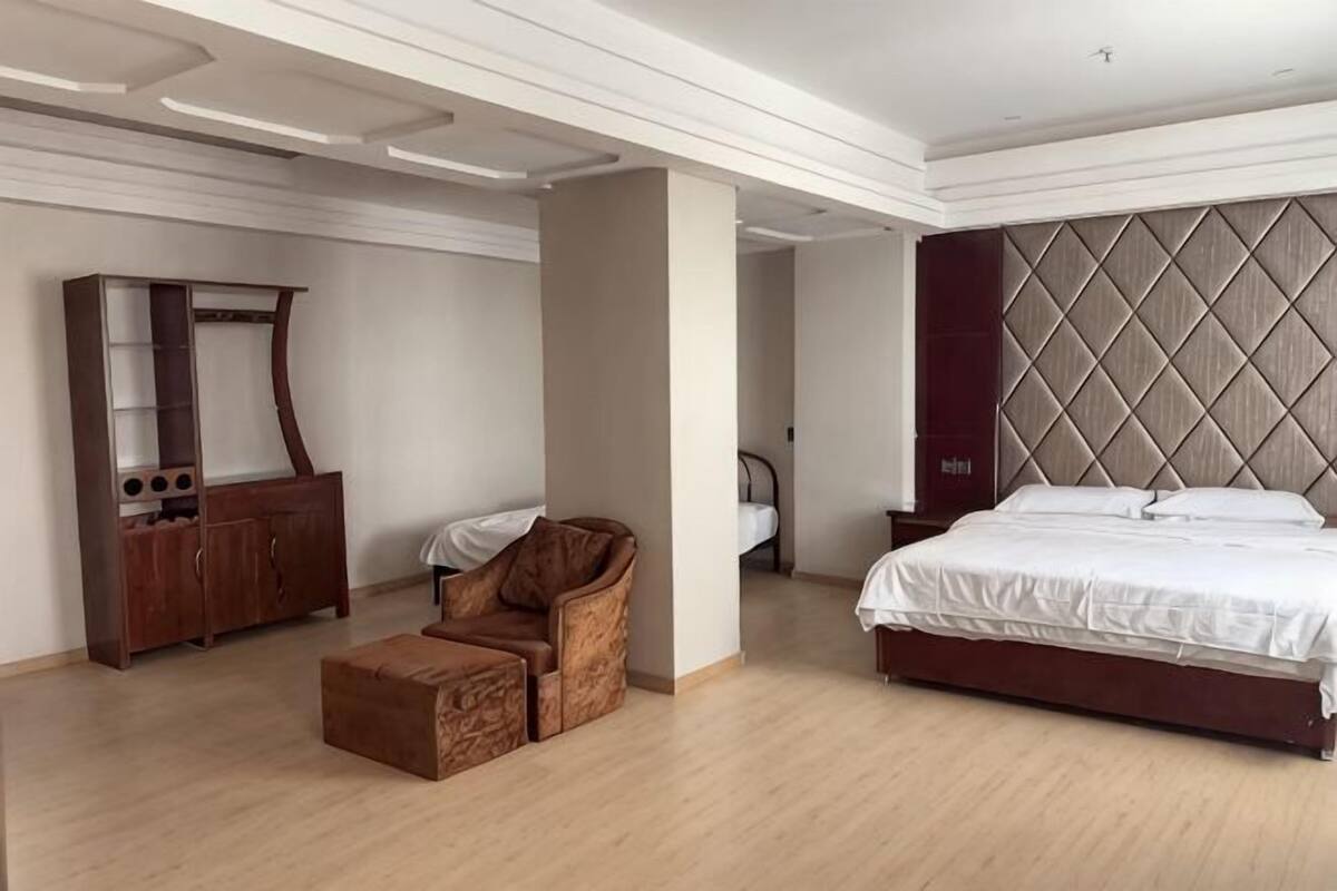 Une chambre à coucher avec un lit, une armoire en bois, un fauteuil brun et un grand miroir.