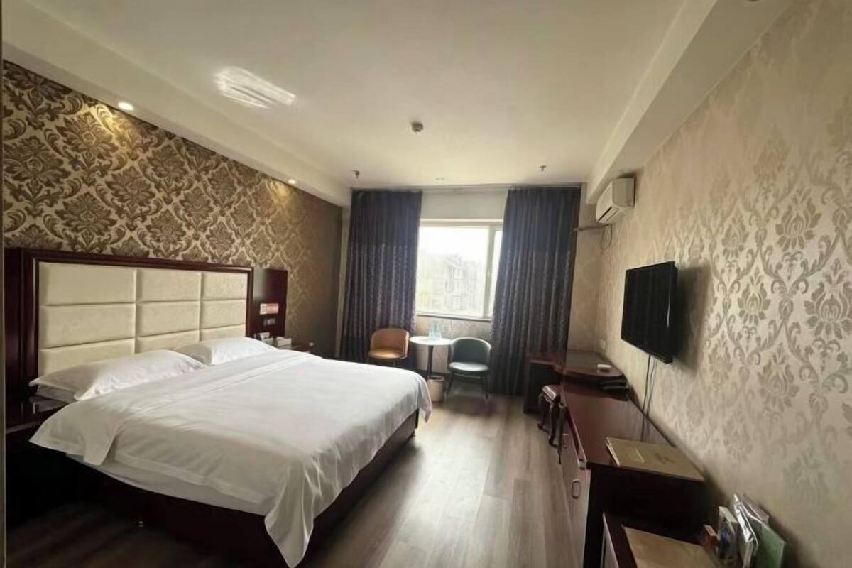 Une chambre d’hôtel avec un grand lit, un bureau, une chaise, une télévision et une fenêtre avec des rideaux.