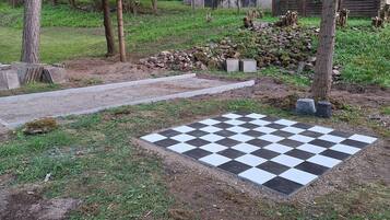 Un espace extérieur à motifs géométriques, avec un chemin pavé et des marches en pierre, entouré d’arbres et d’une pile de bûches.