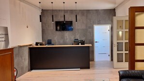 A modern reception area with a desk, a flat-screen TV, pendant lights, and a wooden door. - Hotel am Park (Bad Brueckenau)