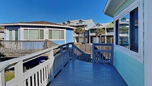 A wooden deck leading to a row of beach houses with balconies and a clear blue sky. - Sunday Villas Sunday Funday by Silver Sands Vacation Rentals (Port Aransas)