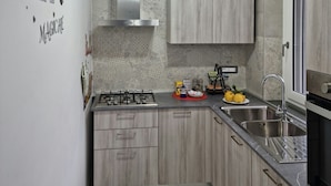 Una cocina moderna con estufa a gas, pileta de acero inoxidable, muebles de madera y detalles decorativos en la pared.