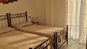 Una cama doble con estructura metálica, una mesita de noche con lámpara y una ventana con cortinas estampadas.