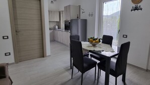 Cocina moderna con armarios de madera clara, un refrigerador gris y un comedor con mesa lista para cuatro comensales.