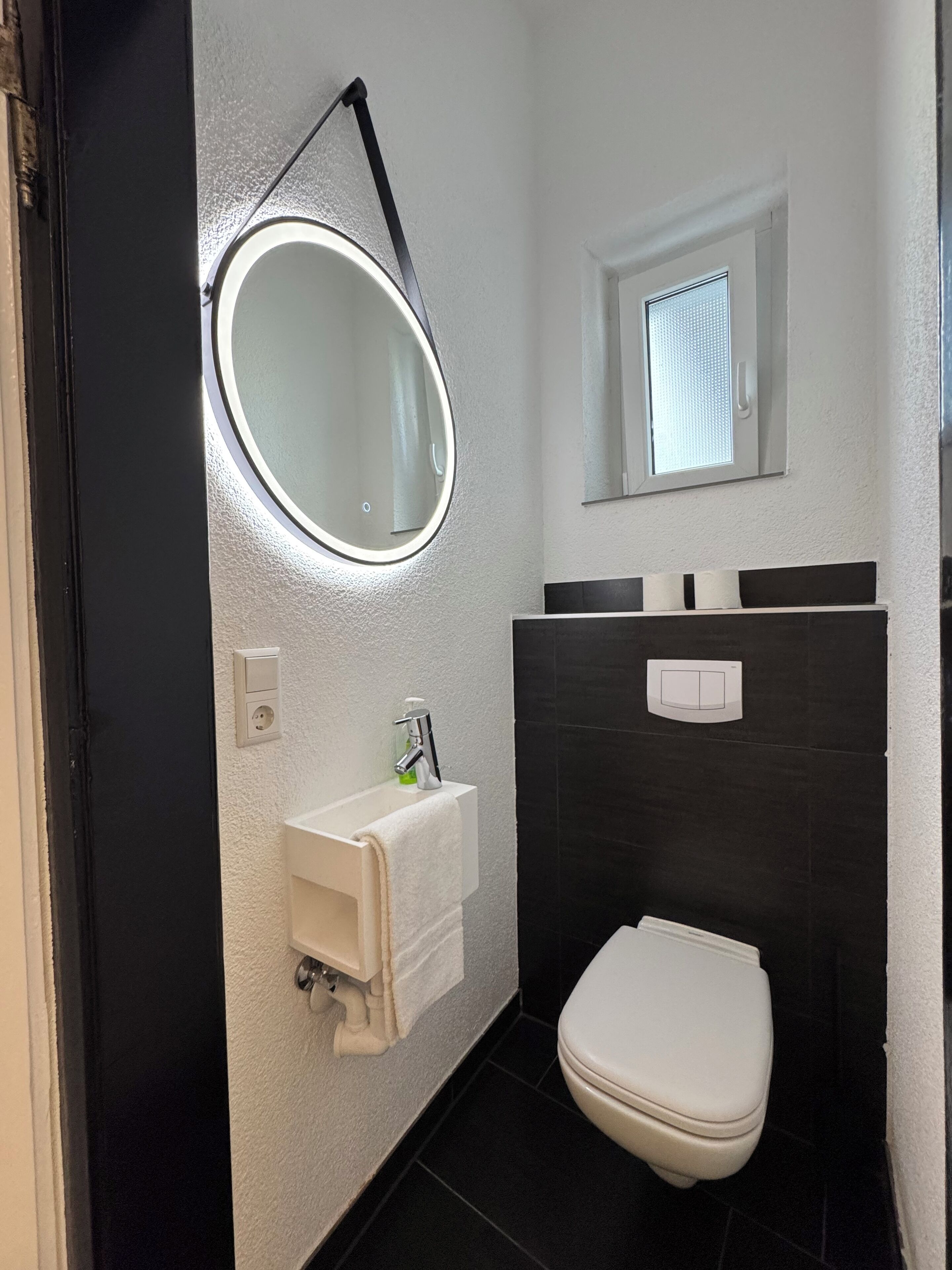 A bathroom with a white sink, a mirror, a toilet, and a window.