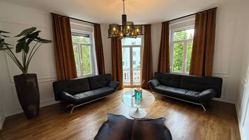 A modern living room with two black sofas, a glass coffee table, a leather rug, and a large potted plant.