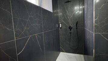 Een moderne badkamer met zwarte marmeren wanden, een witte wastafel en een douchehoek.