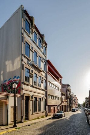 A multi-story building with a red roof, a street with cobblestones, and parked cars.