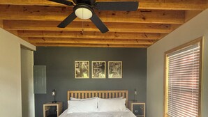 A bedroom with a wooden ceiling, a bed with white bedding, a ceiling fan, and three framed pictures on the wall.