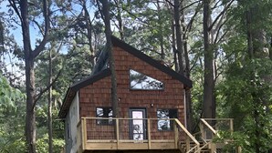 A wooden cabin with a balcony and a staircase, surrounded by trees.