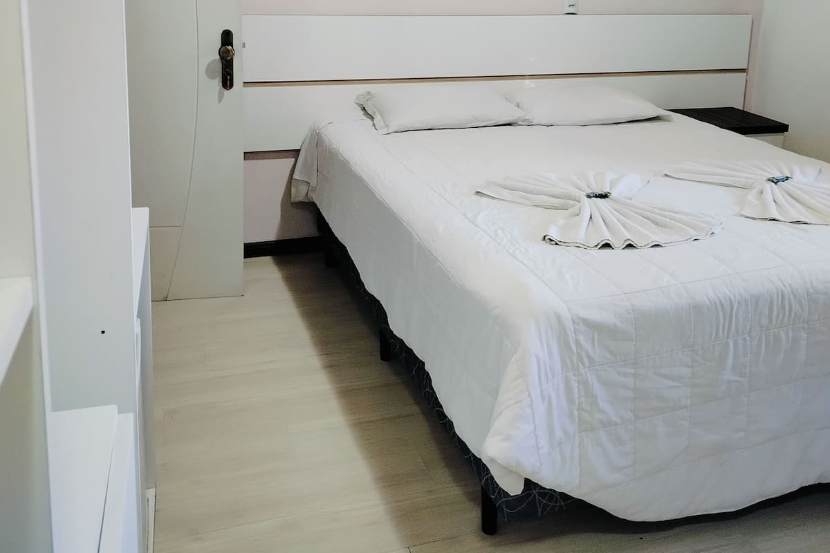 Un dormitorio con cama blanca, cabecero de madera y suelo de tonos claros.
