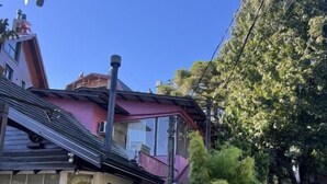 Una casa de dos pisos con un porche delantero, un pequeño jardín y un cielo azul despejado.