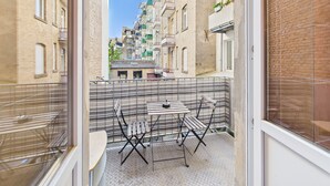 Un balcón con una mesa y sillas, con vistas a una calle estrecha bordeada de edificios.