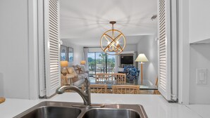 A modern kitchen with a stainless steel sink, a dining area with a glass table, and a view of a balcony with outdoor furniture. - 2BR Golf View Villa Near Beach in Sea Pines Resort (Hilton Head Island)
