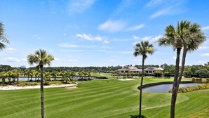 A golf course with palm trees, a pond, and a large building in the background. - 2BR Golf View Villa Near Beach in Sea Pines Resort (Hilton Head Island)