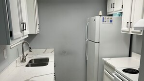Uma cozinha compacta com armários brancos, uma pia de aço inoxidável, uma geladeira e um fogão.