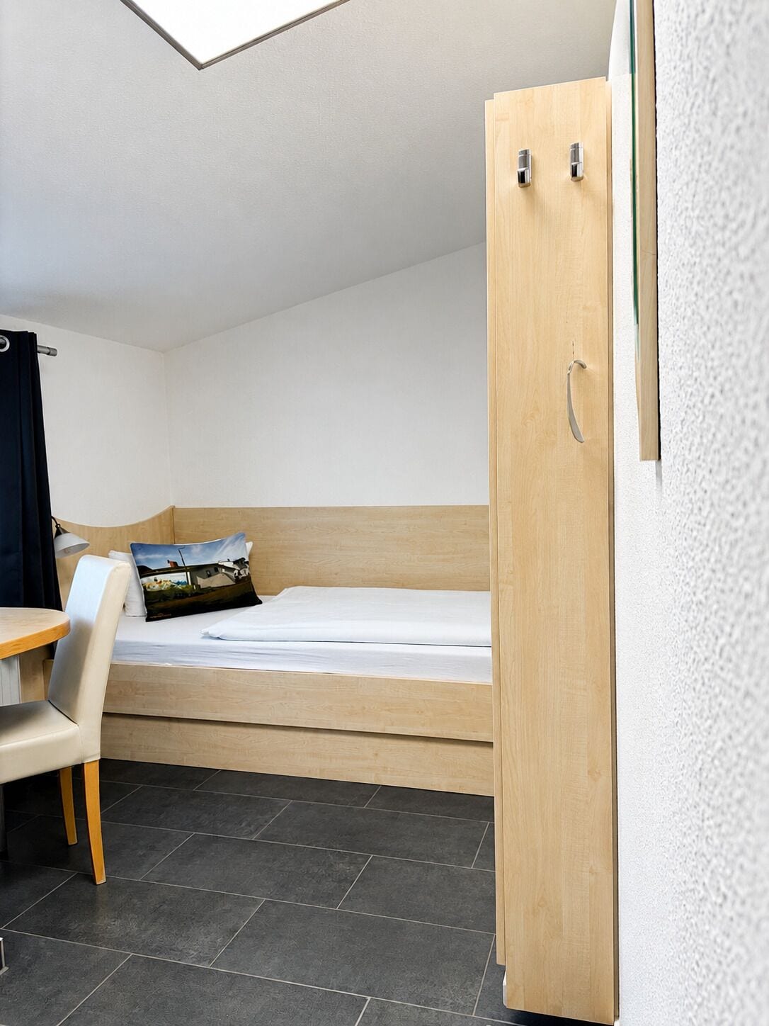 Una habitación pequeña con cama individual, cabecera de madera, escritorio con silla y armario.