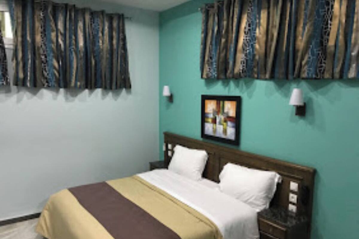 Habitació d'hotel amb un llit, una tauleta de nit, una làmpada i un quadre a la paret.