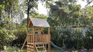 Une cabane en bois avec un toboggan, entourée d’un jardin agrémenté de jardinières surélevées et d’une pelouse.