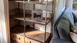 Une étagère métallique dotée de plusieurs compartiments, dont certains contiennent des objets décoratifs, et un livre intitulé « Buitengewoon ».