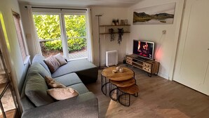 Un salon moderne avec un canapé d’angle gris, une petite table en bois et un téléviseur posé sur un meuble en bois.
