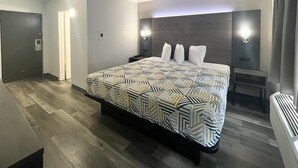 A modern hotel room with a large bed, a nightstand, a wall-mounted lamp, and a door. - Motel 6 - Chicago, IL (Chicago)
